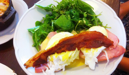 Brunch tradicional con tostada untada en aguacate, huevos fritos y bacon frito